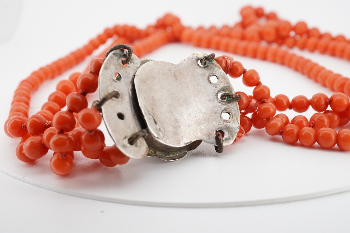 A triple strand graduated coral bead choker necklace, with a cabochon coral set white metal clasp, 38cm.